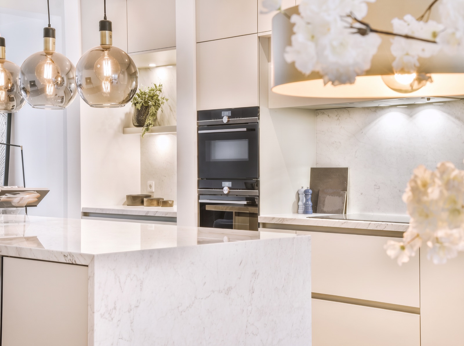 A pale kitchen with a marble island and glass pendant lights
